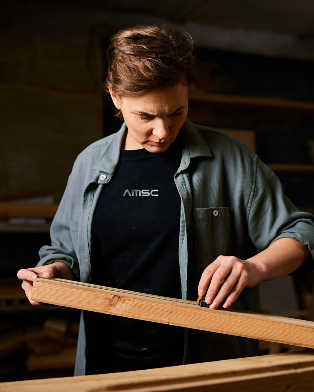 Artisan AMSC mesurant une pièce de bois dans l’atelier